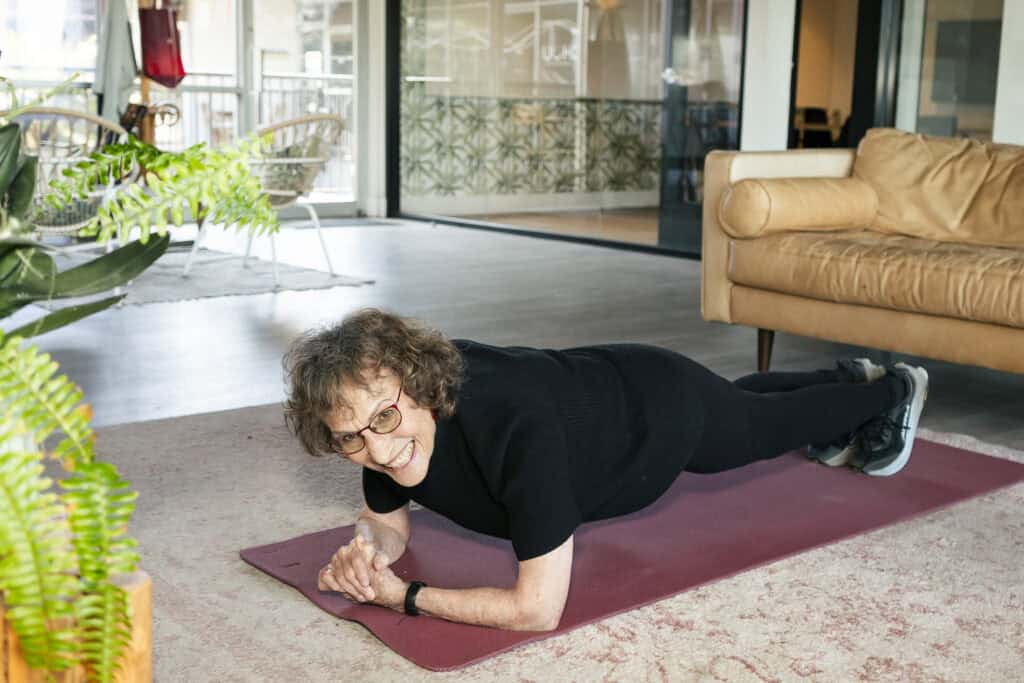 Elderly woman doing a plank in living room.
